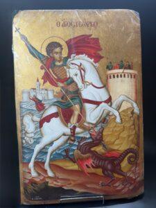 Handpainted Hagiography icon of Saint George. The background is gold colored painted in real wood. The icon can either be hanged on the wall or stand on any surface. Saint George the Troopoephoros or Trophy holder is one of the most famous and beloved saints of Orthodoxy. He came from Cappadocia, martyred and beheaded in 303 AD. His name is related to many folk traditions and customs. Saint George is celebrated on April 23 or the following day after Easter. Size: 59cm (h) x 39cm (w) You can also have the hagiography you desire for your icon corner - iconostasi, gift for your loved ones or your parish. Simply give us all the necessary information (icon theme, dimensions) and we will contact you for further details.